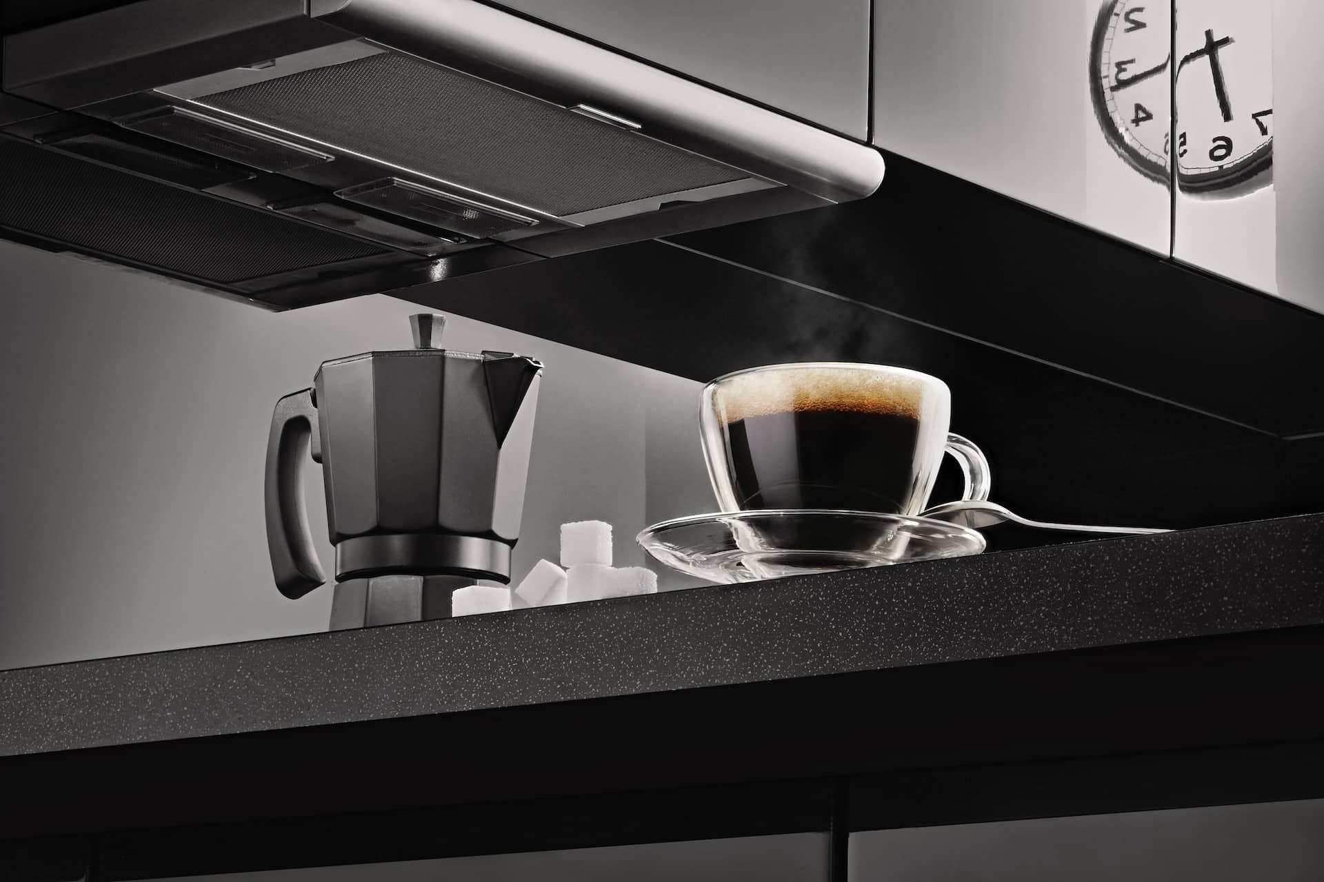 Image shows a Moka pot (or stovetop percolator) on a countertop next to a hot cup of coffee